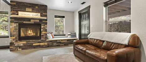 A living room with a stone fireplace, a leather sofa, and a window with a view of trees.