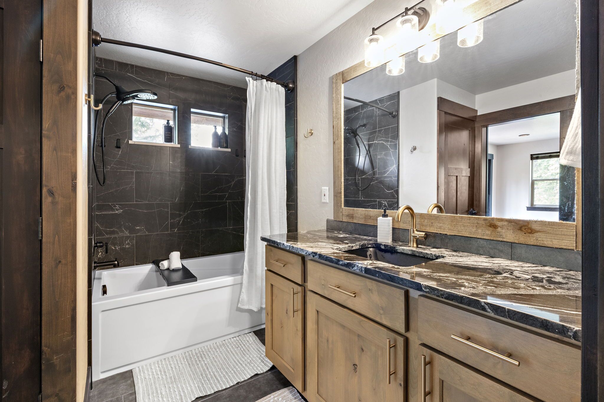 Une salle de bain moderne avec une baignoire, une douche dotée d’une porte en verre, un grand miroir et des meubles en bois.