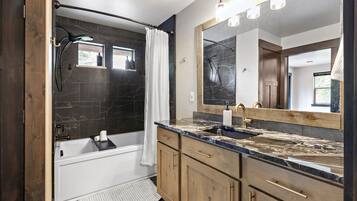 A modern bathroom with a bathtub, a shower with a glass door, a large mirror, and wooden cabinetry.