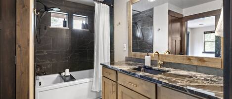 Une salle de bain moderne avec une baignoire, une douche dotée d’une porte en verre, un grand miroir et des meubles en bois.