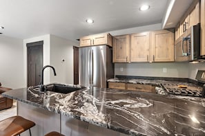 A modern kitchen with a stainless steel refrigerator, wooden cabinets, and a marble countertop.