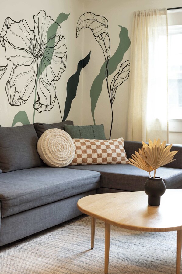 A living room with a grey sofa, a round wooden coffee table, and a wall mural of abstract floral designs.