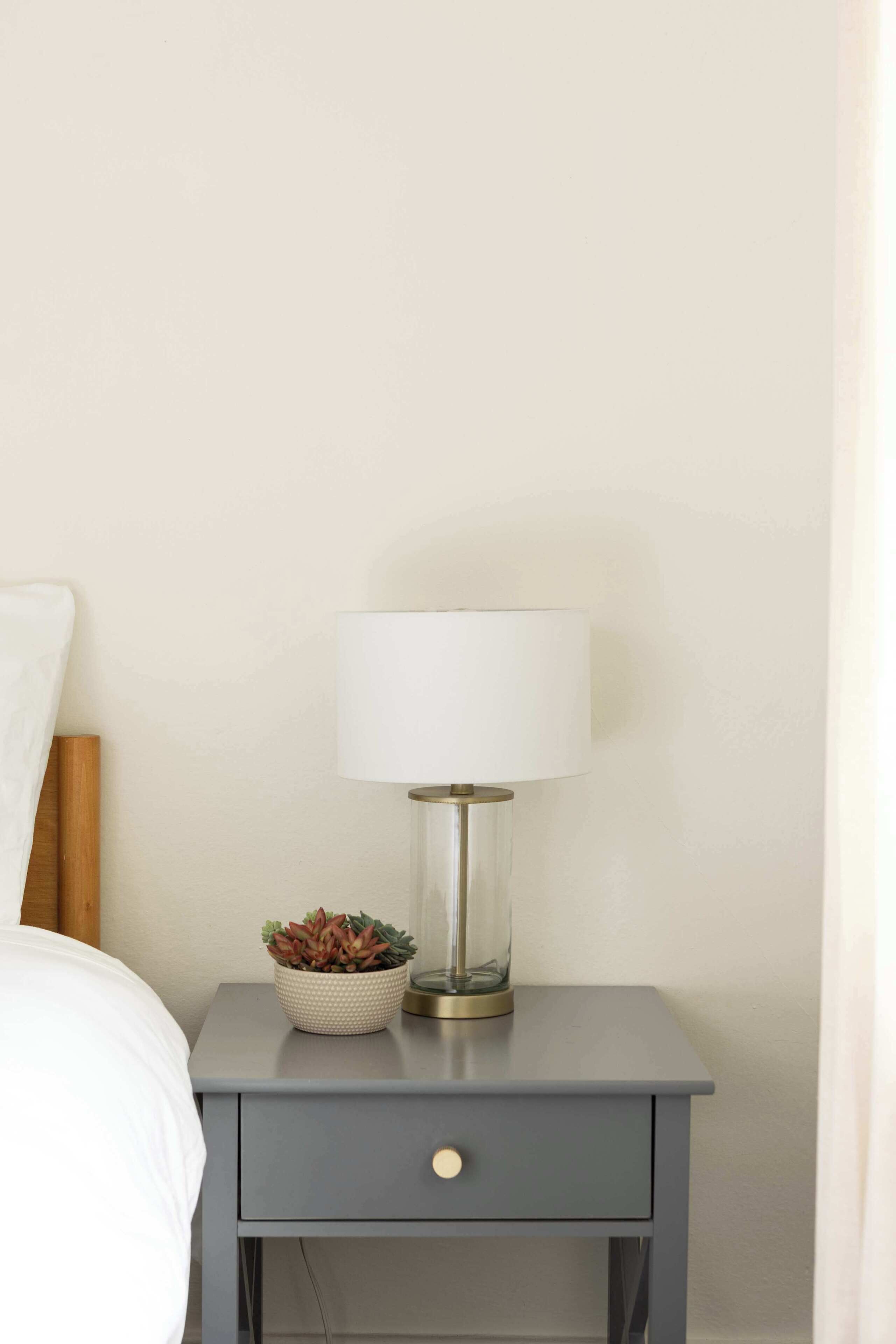 Une petite table de chevet avec une lampe et une plante, placée contre un mur uni.