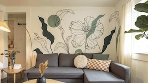 A modern living room with a grey sofa, a round wooden coffee table, and a wall mural of abstract floral designs. - Historic Flat in Downtown Boise (Boise)