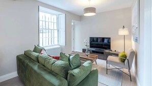 Ein Wohnzimmer mit einem grünen Sofa, einem Couchtisch, einem Fernseher und einer Stehlampe.