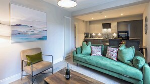 Ein modernes Wohnzimmer mit einem grünen Sofa, einem Couchtisch aus Holz mit einer Flasche und Gläsern, einem Sessel und einem großen abstrakten Gemälde an der Wand.