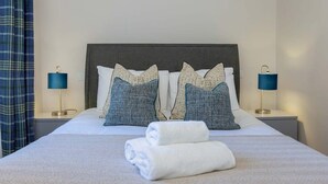 Una cama bien hecha con almohadas, una toalla doblada y dos lámparas de noche.