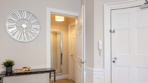 Un pasillo con una puerta blanca, un reloj de pared blanco y una pequeña mesa con objetos encima.
