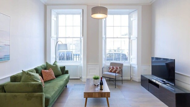 Una sala de estar moderna con un sofá verde, una mesa de centro, un televisor y ventanas grandes.