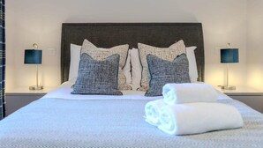 A neatly made bed with a grey headboard, two bedside lamps, and a folded white towel on the bed. - Edinburgh City Centre 2 Bed Apartment (Edinburgh)
