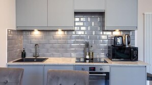 A modern kitchen with grey cabinets, a tiled backsplash, a built-in microwave, and a toaster. - Edinburgh City Centre 2 Bed Apartment (Edinburgh)