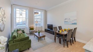 A modern living room with a green sofa, dining table, and chairs, a TV, and large windows. - Edinburgh City Centre 2 Bed Apartment (Edinburgh)