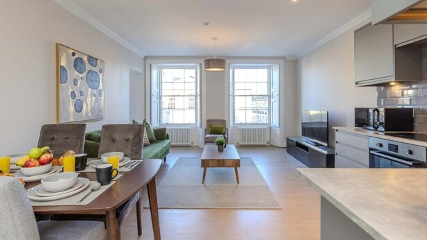 Een moderne woonkamer met een eettafel, bank en keuken voorzien van apparatuur.