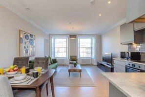 Un salon moderne comprenant une table à manger, un canapé et un coin cuisine équipé d’appareils électroménagers.