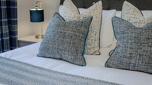 Een net opgemaakt bed met patroon kussens en een lamp op een nachtkastje.