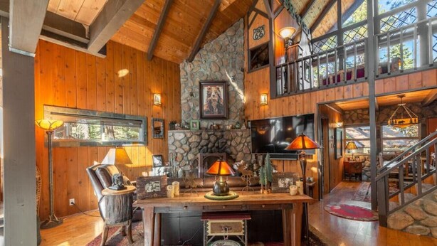A rustic interior with a stone fireplace, wooden beams, and a large TV mounted on the wall. - Rustic Beauty in Chamberlands Full Beach & Pool (Homewood)