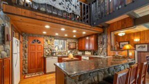 A spacious kitchen with a large island, wooden cabinets, and a stone accent wall. - Rustic Beauty in Chamberlands Full Beach & Pool (Homewood)
