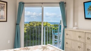 A bedroom with a large sliding glass door leading to a balcony with a view of greenery and the ocean. - Marina to Ocean View Key Largo Ocean Pointe 5308 (Tavernier)