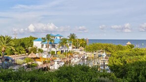 A coastal property with a marina, a large house with a blue roof, and lush greenery. - Marina to Ocean View 2BR | Ocean Pointe 5308 (Tavernier)