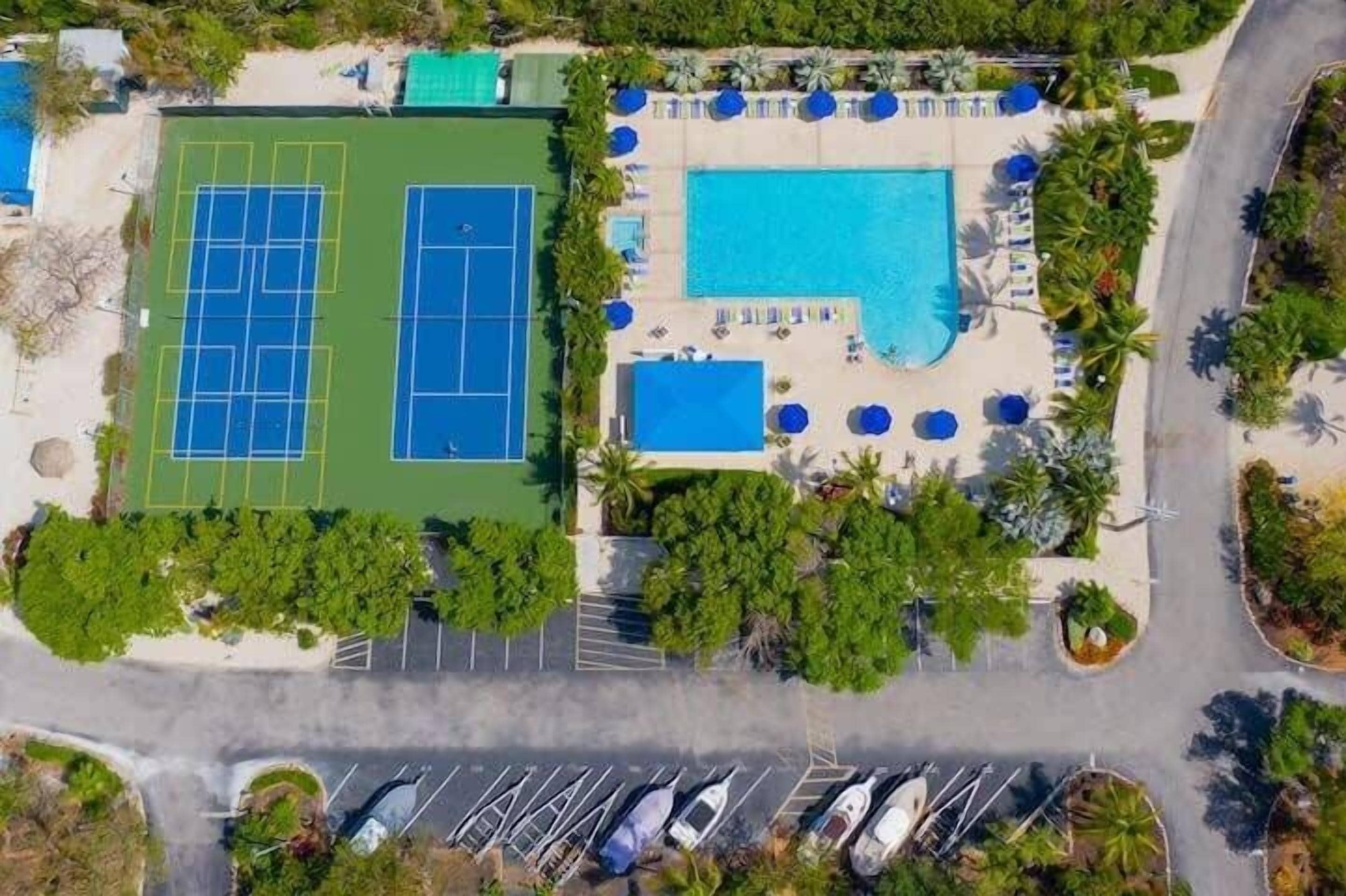 An aerial view of a resort with tennis courts, a swimming pool, and a parking area.