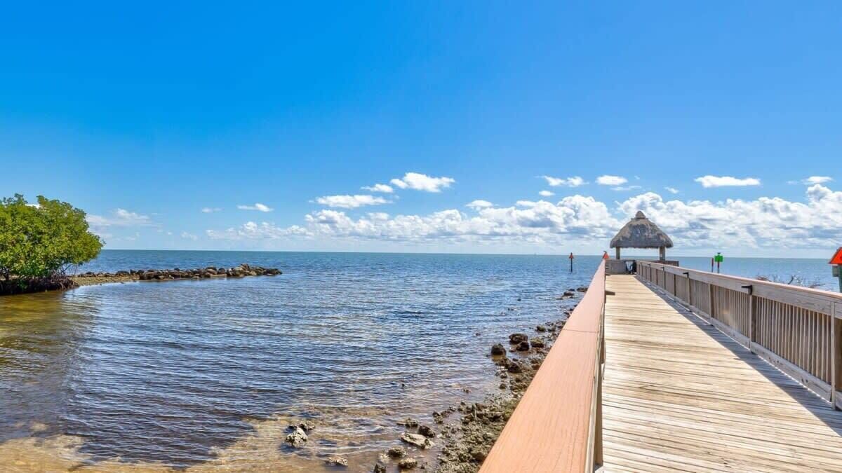 A wooden pier extending into calm waters with a thatched-roof structure at the end.