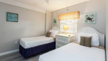 A bedroom with two single beds, a bedside table with a lamp, and a window with blinds.