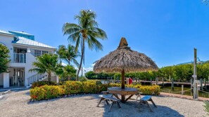 A beachside area with a thatched umbrella, a wooden table, and benches. - Marina to Ocean View Key Largo Ocean Pointe 5308 (Tavernier)