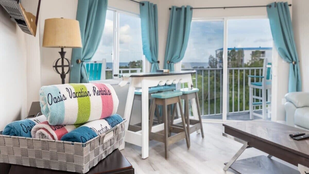 A cozy room with a bed, a table, and a chair. There's a view of the outdoors through large windows.