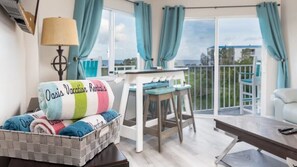 A cozy room with a bed, a table, and a chair. There's a view of the outdoors through large windows. - Marina to Ocean View Key Largo Ocean Pointe 5308 (Tavernier)