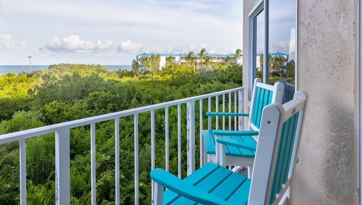A balcony with turquoise chairs and a view of a lush green landscape and a distant building.