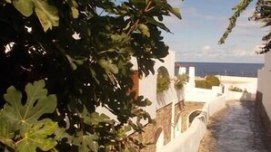 A narrow stone pathway leading to a white building with arches, overlooking a body of water.