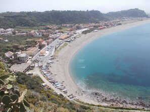 Una cittadina costiera con spiaggia fiancheggiata da barche ormeggiate e una strada che corre parallela alla costa.
