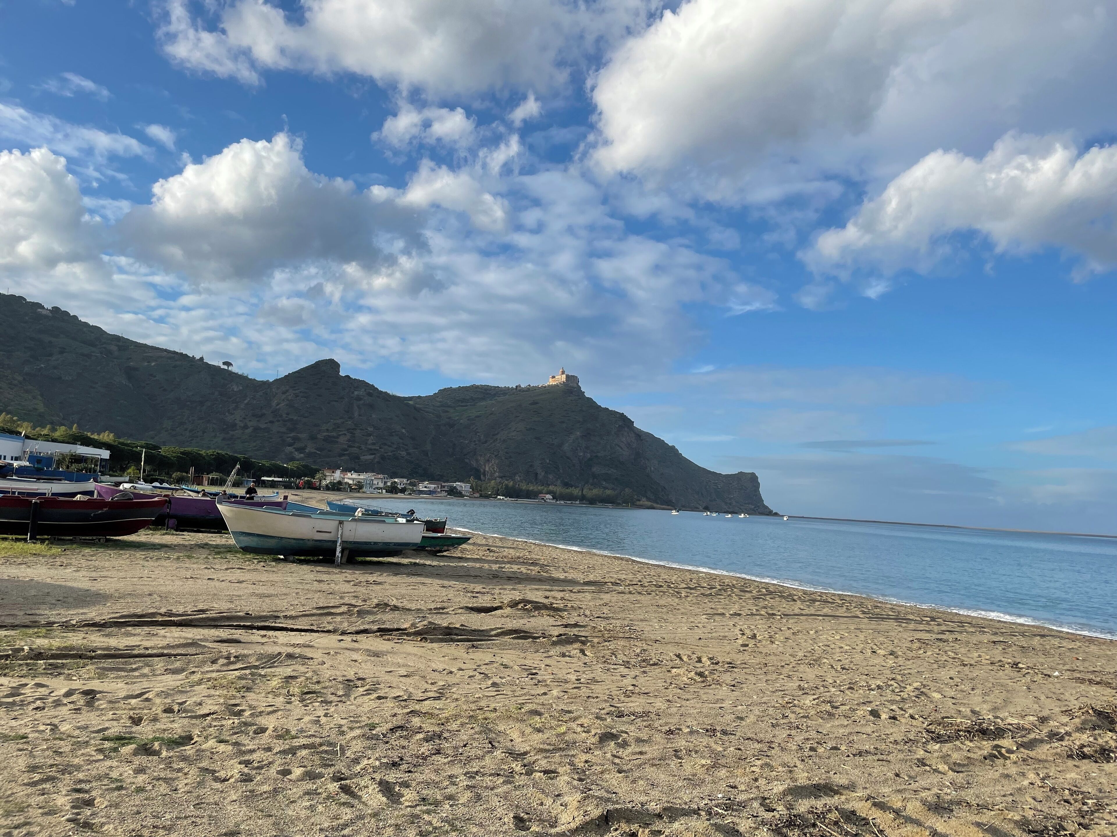 A beach with boats, a mountain, and a castle.