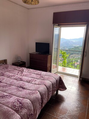 Relax in this serene bedroom with a large bed, flat-screen TV, and sliding glass door leading to a balcony with a breathtaking mountain view.
