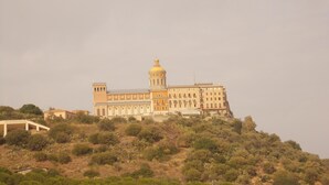 A large, historic building with a prominent tower and dome, situated on a hill with surrounding vegetation.