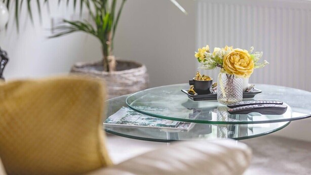 A glass coffee table with a vase of yellow flowers, a small statue, and a remote control. - Stylish 3-Bed House in Langley|Drive - By Tempstay (Berkshire)