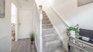 A staircase with a white railing, a door at the top, and a console table with a plant and a box. - Stylish 3-Bed House in Langley|Drive - By Tempstay (Berkshire)