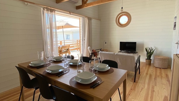 Un comedor con una mesa de madera preparada para cuatro personas, rodeada de sillas negras. Un televisor está montado en la pared a la derecha.