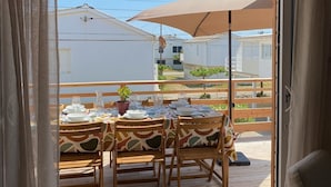 Una terraza de madera con una mesa lista para comer, una planta en maceta y una sombrilla.