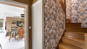 A modern kitchen with wooden cabinets, a dining area with a table and chairs, and a staircase with a leaf-patterned wallpaper.