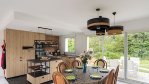 A modern kitchen with wooden cabinets, a dining area with a table set for four, and a large sliding glass door leading to a garden.