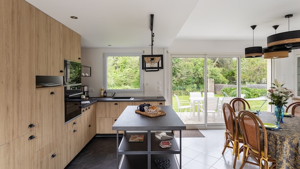 A modern kitchen with wooden cabinets, a built-in oven, and a dining area with a table and chairs.