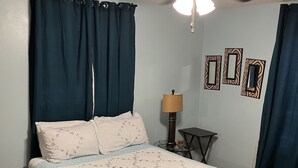 A bedroom with a bed, curtains, a ceiling fan, a lamp, and wall art. - Lake house with access to the best beach for swimming & fishing on Lake Hamilton (Hot Springs)