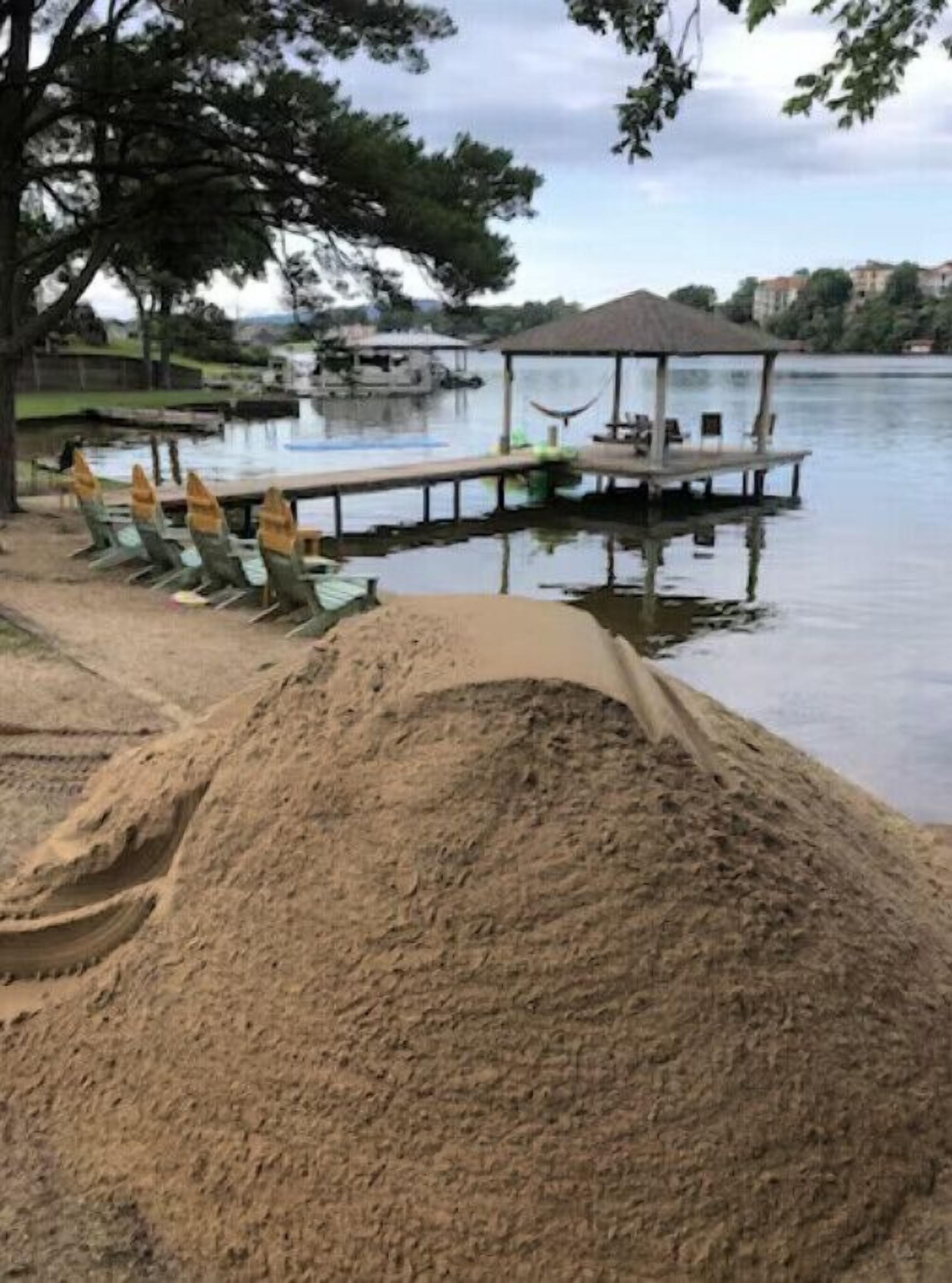 Una zona junto al lago con una playa de arena, un área de estar cubierta con sillas y un muelle que se adentra en el agua.