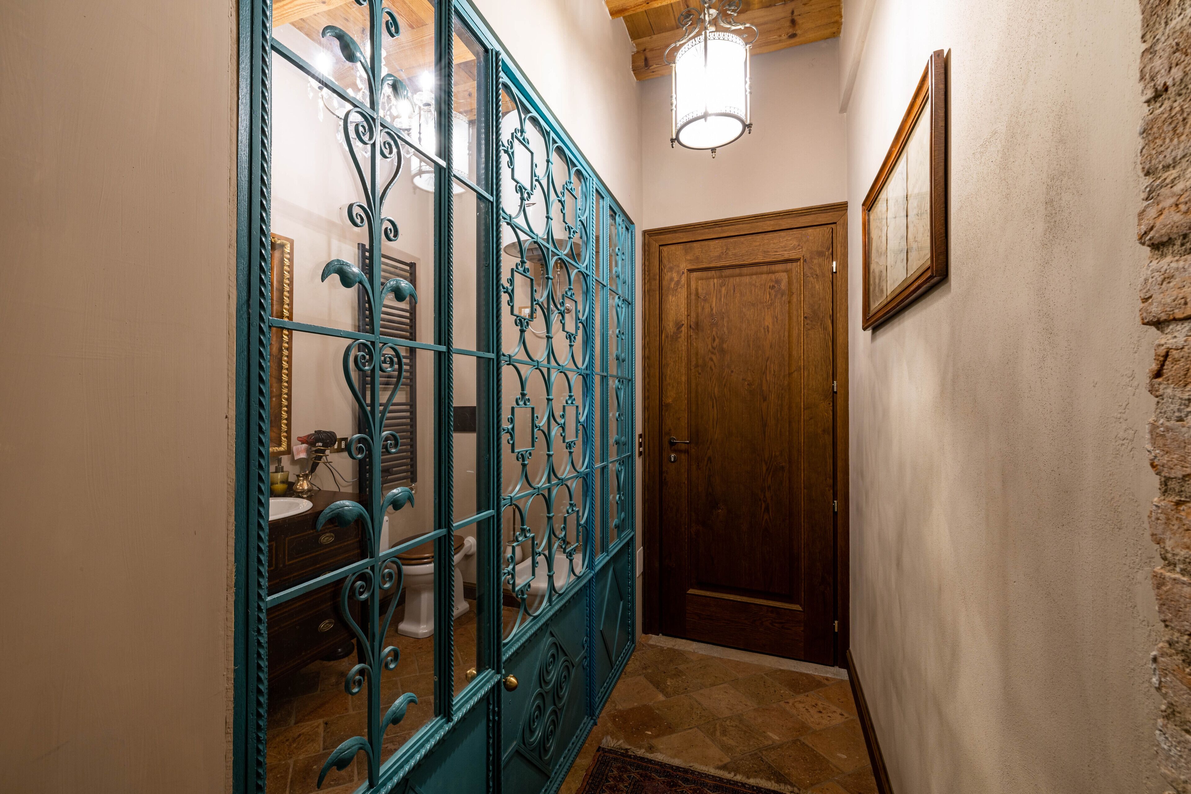 A hallway with a wooden door, a blue metal gate, and a framed picture on the wall.