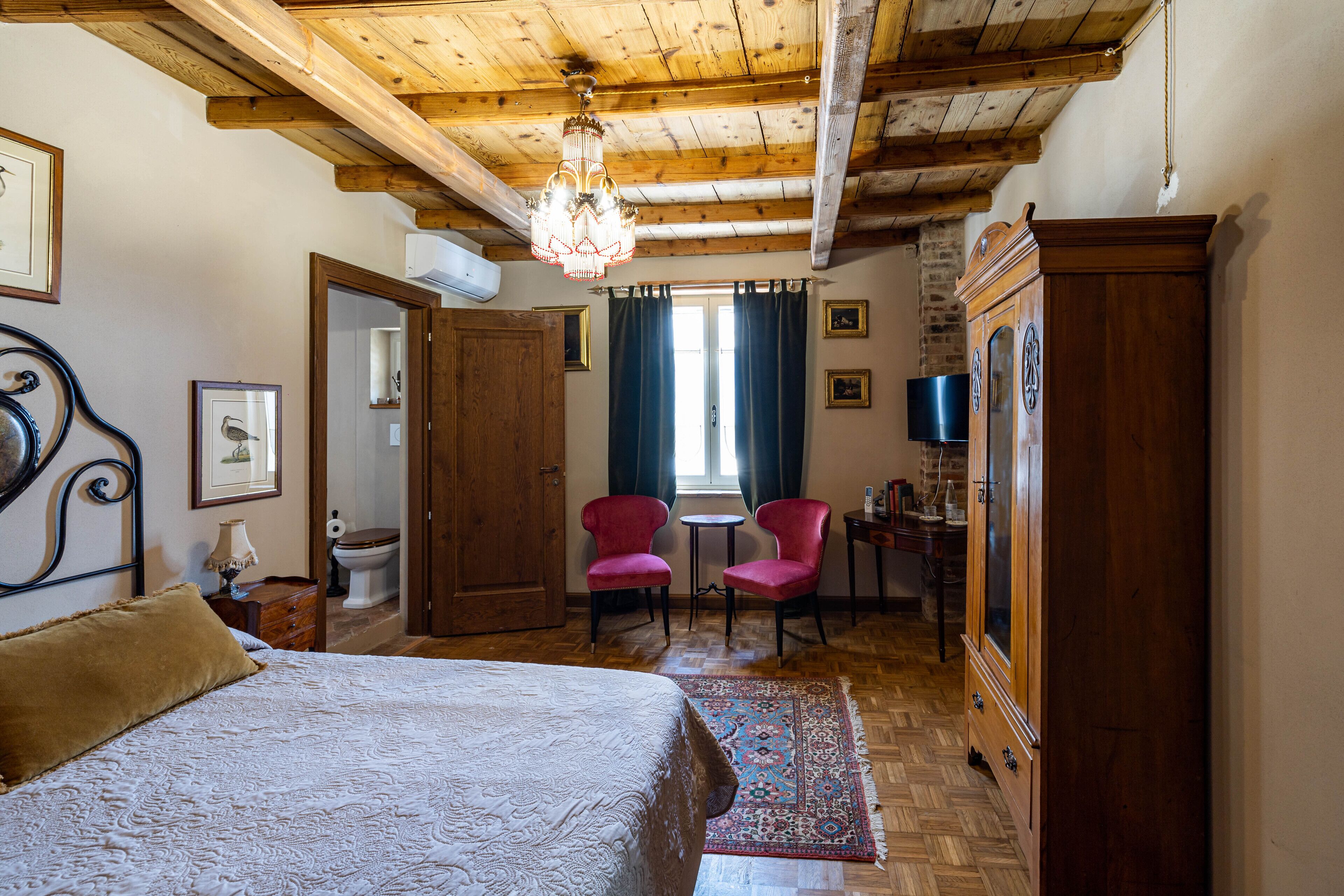 A bedroom with a wooden ceiling, a bed, a chandelier, a wooden wardrobe, and a small table with chairs.