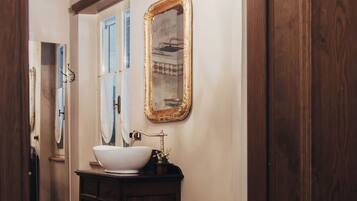 Een badkamer met een houten vloer, een witte wastafel, een bidet en een spiegel met gouden lijst.