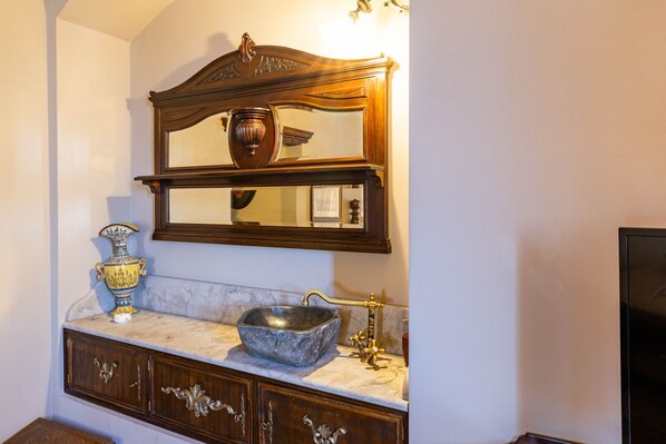 A bathroom with a marble sink, a decorative vase, and a mirror above the sink.
