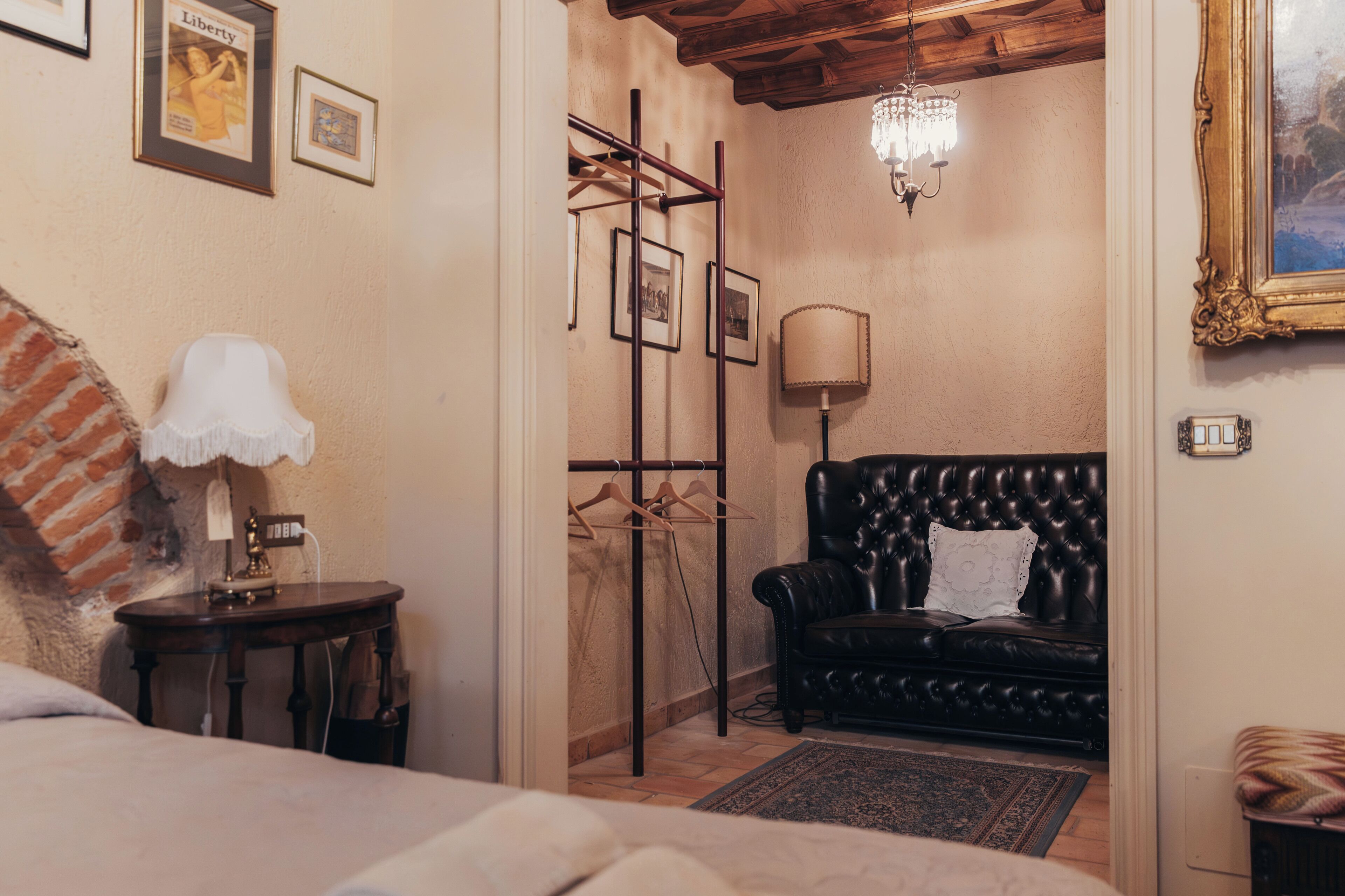Ein Zimmer mit einem Bett, einem schwarzen Ledersofa, einem Holztisch mit einer Lampe, einem Kleiderständer und einem Kronleuchter.
