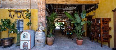 A narrow alleyway with a yellow building, potted plants, and a wooden barrel.